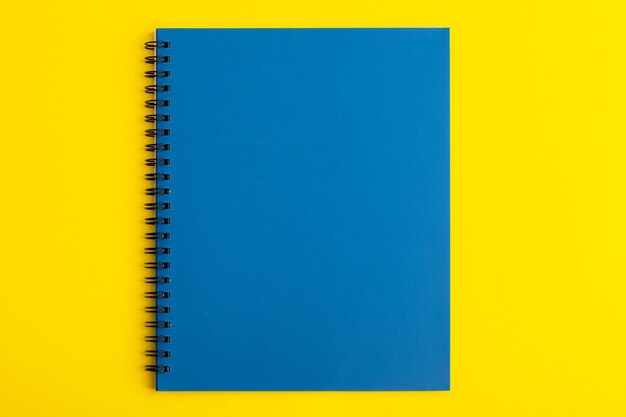 Vista frontal cuaderno azul abierto sobre escritorio amarillo