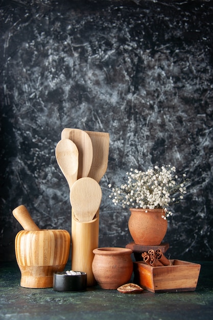 Vista frontal de cucharas de madera con ollas y canela en la pared oscura condimentos de color fotográfico cubiertos de comida salada