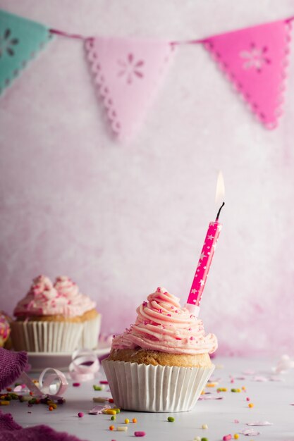 Vista frontal de cupcake de cumpleaños con guirnaldas y velas encendidas