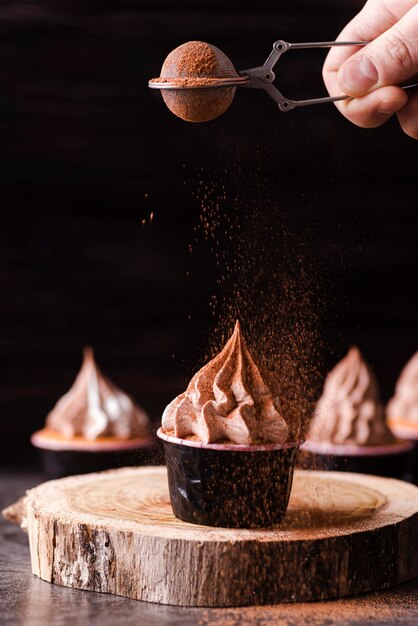 Vista frontal de cupcakes con persona tamizando polvo de cacao en la parte superior