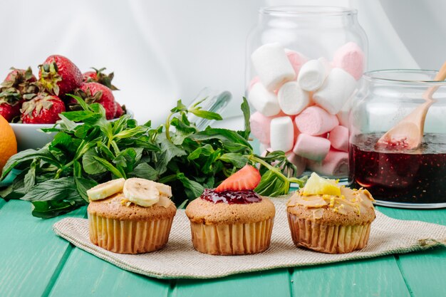 Vista frontal de cupcakes con plátanos, fresas, limón y menta con malvaviscos en un frasco