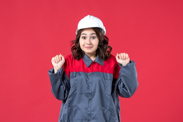 Vista frontal de la curiosa constructora en uniforme con casco sobre fondo rojo aislado