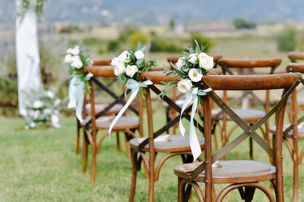 Vista frontal de la decoración floral de eustomas blancas y ruscus de sillas chiavari marrones al aire libre