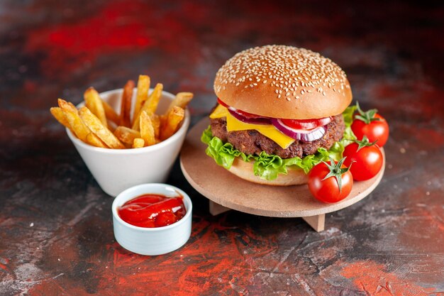 Vista frontal deliciosa carne hamburguesa con queso con papas fritas y tomates sobre fondo marrón oscuro comida rápida cena plato sándwich bocadillo tostada