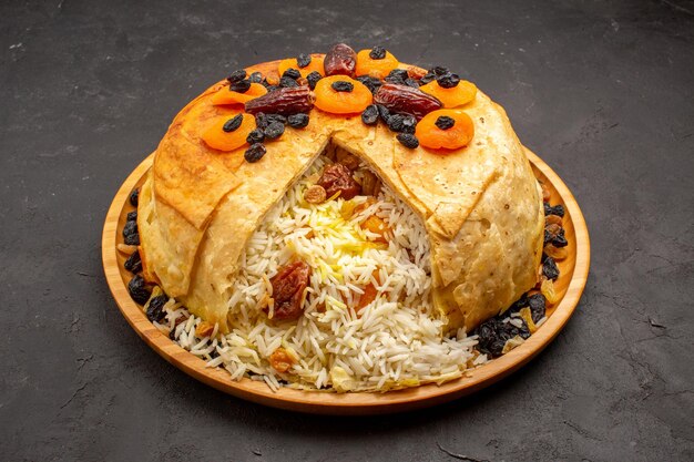 Vista frontal de la deliciosa comida de arroz shakh plov cocinada dentro de masa redonda con pasas en el espacio gris