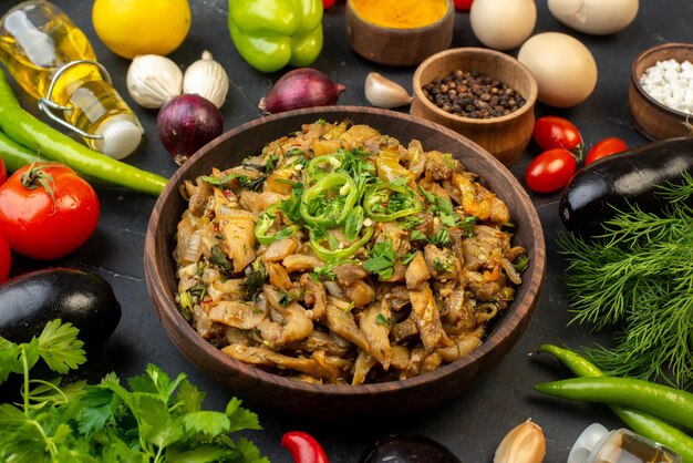 Vista frontal de la deliciosa comida de berenjena, verduras frescas, especias, botella de aceite caída, paquete verde sobre fondo de color oscuro