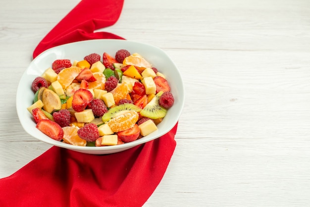 Vista frontal deliciosa ensalada de frutas con tejido rojo sobre una superficie blanca cítricos exóticos frutos rojos maduros suaves