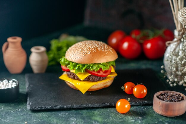 Vista frontal deliciosa hamburguesa de carne con tomates rojos sobre fondo oscuro