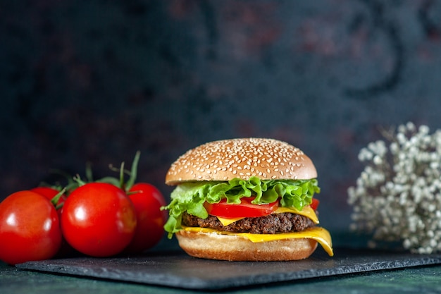 Vista frontal deliciosa hamburguesa de carne con tomates rojos sobre fondo oscuro