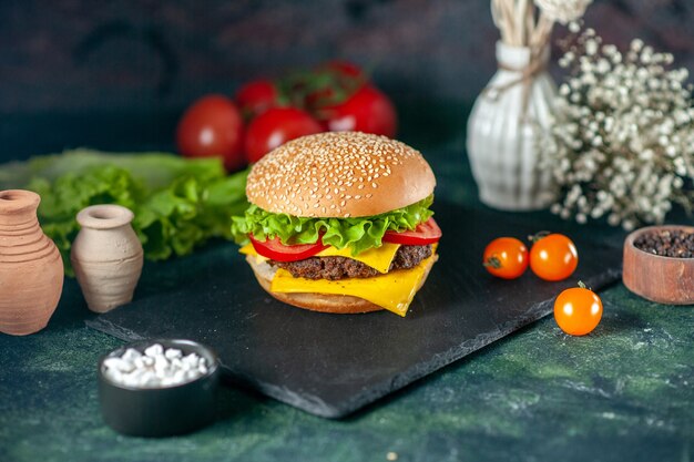 Vista frontal deliciosa hamburguesa de carne con tomates rojos sobre fondo oscuro
