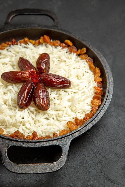 Vista frontal deliciosa harina de arroz cocido plov con pasas dentro de la sartén en la superficie oscura comida arroz comida oriental cena