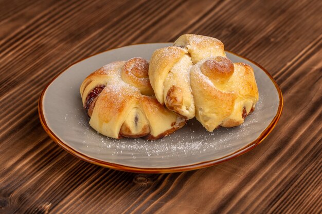 Vista frontal deliciosa pastelería con relleno dentro de la placa sobre la mesa de madera, pastel de azúcar dulce hornear fruta de pastelería