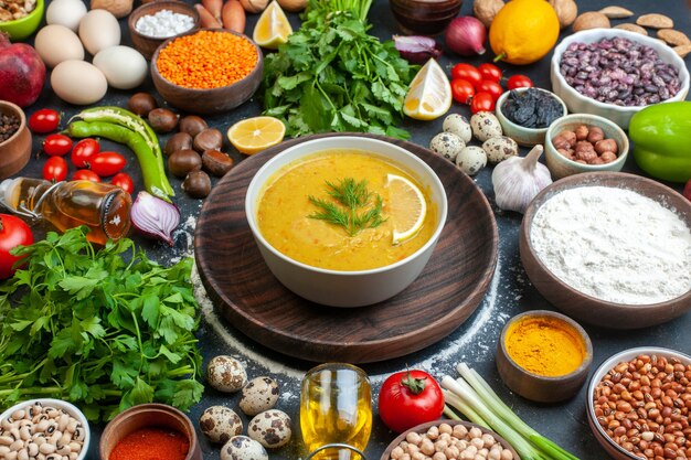 Vista frontal de la deliciosa sopa servida con limón y verde en un recipiente blanco en la bandeja de madera, verduras, alimentos, botella de aceite, especias en el cuadro negro