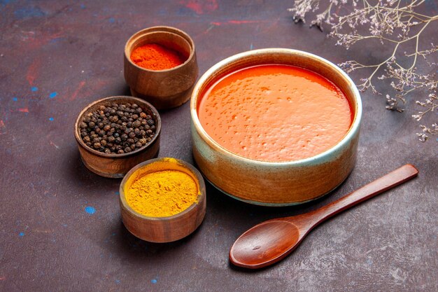 Vista frontal deliciosa sopa de tomate cocinada con tomates frescos con condimentos en el espacio oscuro