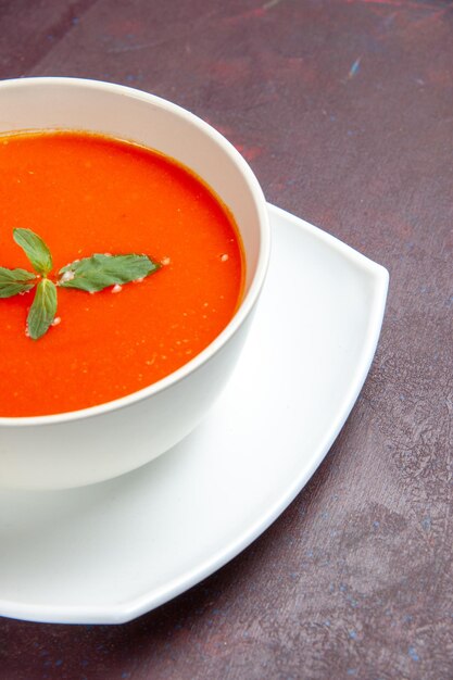 Vista frontal deliciosa sopa de tomate sabroso plato con una sola hoja dentro de la placa en el escritorio oscuro plato salsa tomate color sopa