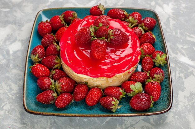 Vista frontal deliciosa tarta de pastel con crema roja y fresas frescas sobre una superficie blanca clara