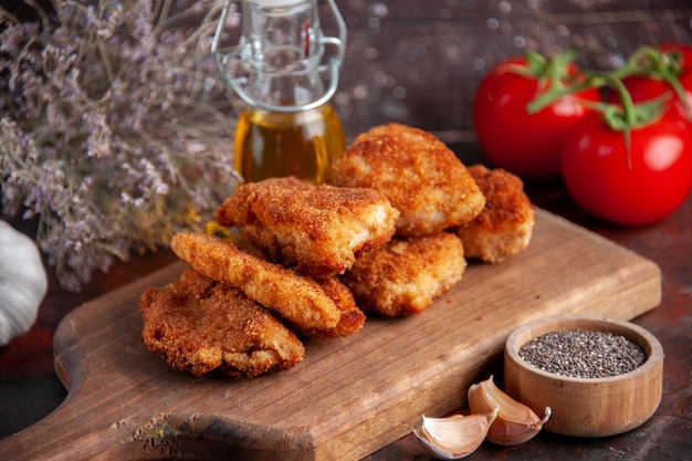 Vista frontal deliciosas alitas de pollo en la tabla de cortar con tomates fondo oscuro cena sándwich comida hamburguesa ensalada almuerzo