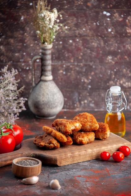 Vista frontal deliciosas alitas de pollo en la tabla de cortar con tomates fondo oscuro hamburguesa comida comida sándwich almuerzo ensalada horizontal