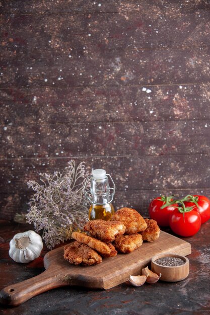 Vista frontal deliciosas alitas de pollo en la tabla de cortar con tomates superficie oscura