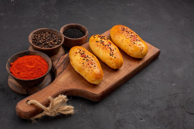 Vista frontal deliciosas empanadas recién horneadas del horno con condimentos sobre fondo gris horno de tarta pastelería pastel de carne hornear