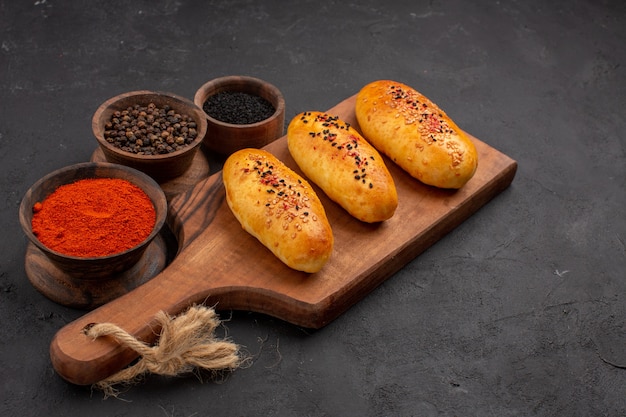 Vista frontal deliciosas empanadas recién horneadas del horno con condimentos sobre fondo gris horno de tarta pastelería pastel de carne hornear