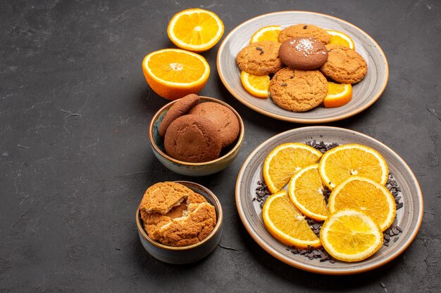 Vista frontal deliciosas galletas de arena con naranjas frescas en rodajas sobre fondo oscuro galleta de azúcar galleta dulce pastel de frutas