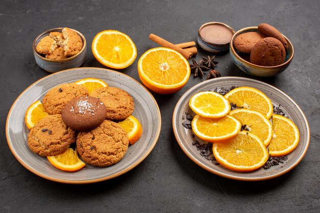 Vista frontal deliciosas galletas de arena con naranjas frescas en rodajas sobre fondo oscuro galleta de fruta dulce color cítrico de azúcar de galleta