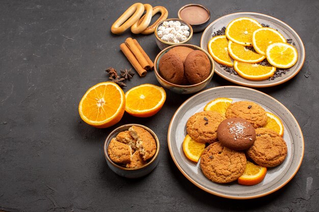 Vista frontal deliciosas galletas de arena con naranjas frescas sobre fondo oscuro galleta de azúcar galleta de frutas cítricos dulces