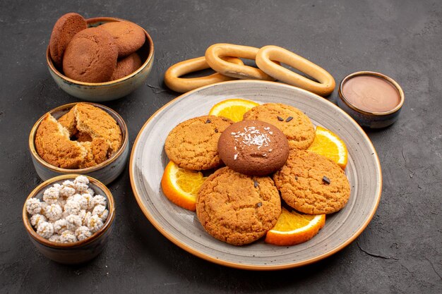 Vista frontal deliciosas galletas de azúcar con naranjas frescas en rodajas sobre fondo oscuro galleta galleta postre pastel de azúcar dulce