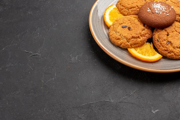 Vista frontal deliciosas galletas de azúcar con naranjas en rodajas dentro de la placa sobre fondo oscuro galleta de azúcar galletas dulces fruta