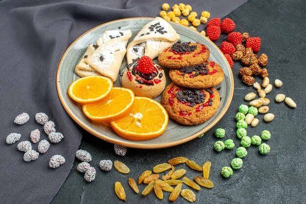Vista frontal deliciosas galletas de azúcar con pasteles y rodajas de naranja en la superficie oscura galleta de azúcar dulce pastel de té galleta