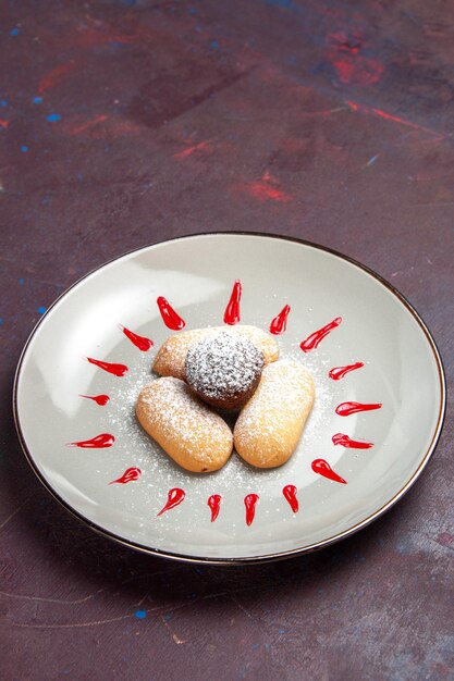 Vista frontal deliciosas galletas con azúcar en polvo y glaseado rojo dentro de la placa en el espacio oscuro