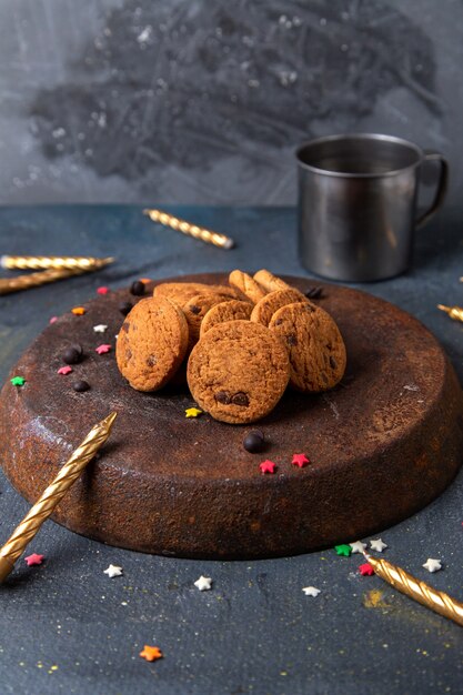 Vista frontal de deliciosas galletas de chocolate con velas en la superficie gris oscuro