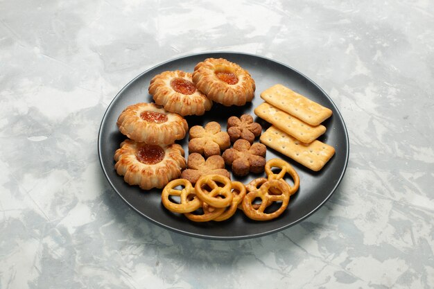 Vista frontal deliciosas galletas con galletas saladas y patatas fritas dentro de la placa en el escritorio de color blanco claro