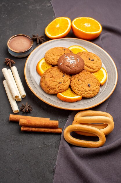 Vista frontal deliciosas galletas con naranjas frescas en rodajas sobre el fondo oscuro galleta de azúcar galleta de fruta dulce