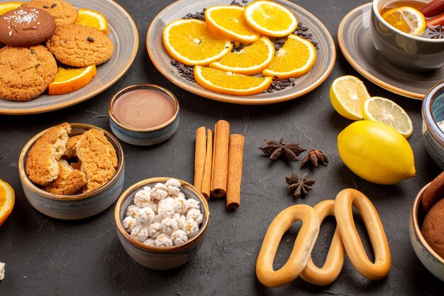 Vista frontal deliciosas galletas con naranjas frescas y té sobre fondo oscuro galleta de azúcar galleta de fruta dulce