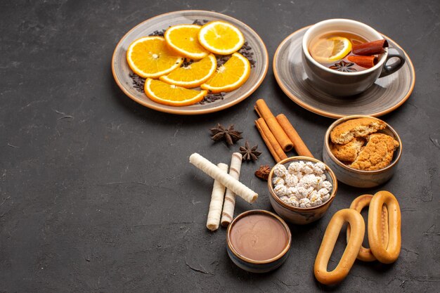 Vista frontal deliciosas galletas con naranjas en rodajas y una taza de té sobre el fondo oscuro galleta de azúcar galleta dulce de frutas