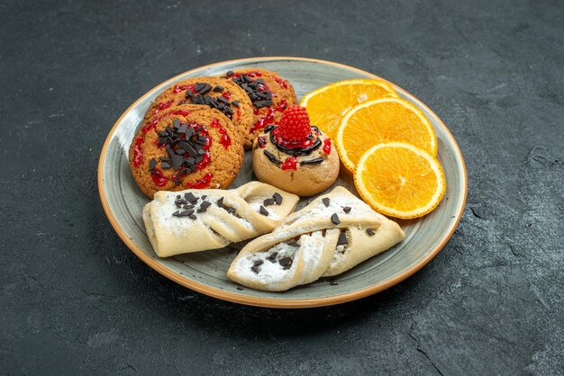 Vista frontal deliciosas galletas con pasteles afrutados y rodajas de naranja sobre la superficie oscura pastel dulce de frutas pastel té azúcar