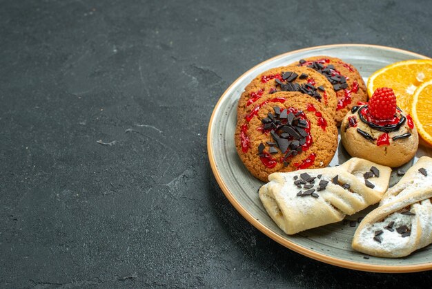 Vista frontal deliciosas galletas con pasteles afrutados y rodajas de naranja en la superficie oscura de frutas pastel dulce té azúcar