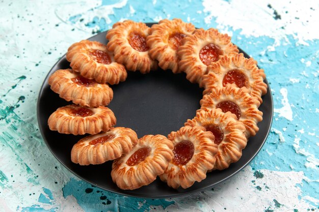 Vista frontal deliciosas galletas redondas formadas con mermelada dentro de la placa negra en la pared azul claro pastel de galleta dulce de azúcar de galleta