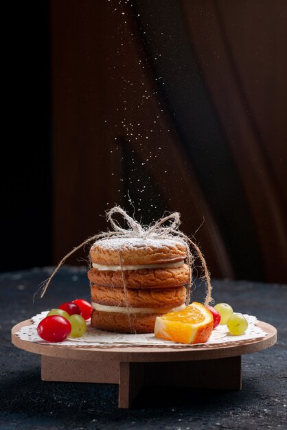 Vista frontal deliciosas galletas sándwich atadas deliciosas con frutas en rodajas obteniendo azúcar en polvo en el pastel de escritorio azul oscuro