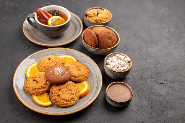 Vista frontal deliciosas galletas con una taza de té y naranjas sobre fondo oscuro galleta fruta dulce pastel cookie cítricos