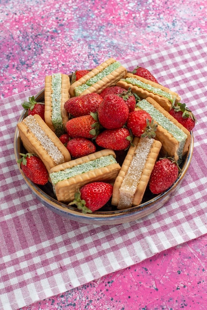 Vista frontal de deliciosas galletas waffle con fresas rojas frescas en la pared rosa