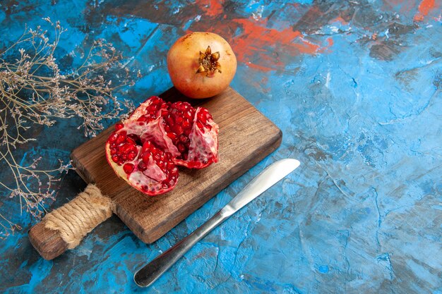 Vista frontal deliciosas granadas en tabla de cortar, cuchillo de cena en abstracto azul con espacio libre