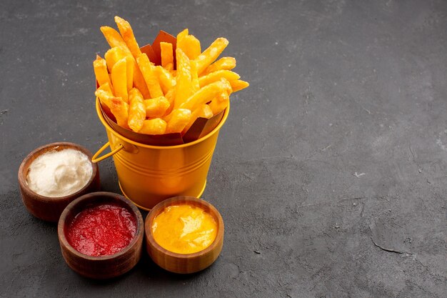 Vista frontal deliciosas papas fritas con condimentos en el espacio oscuro