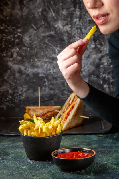 Vista frontal deliciosas papas fritas con condimentos que se comen por la superficie oscura femenina