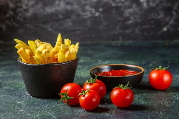 Vista frontal deliciosas papas fritas con tomates cherry en superficie oscura