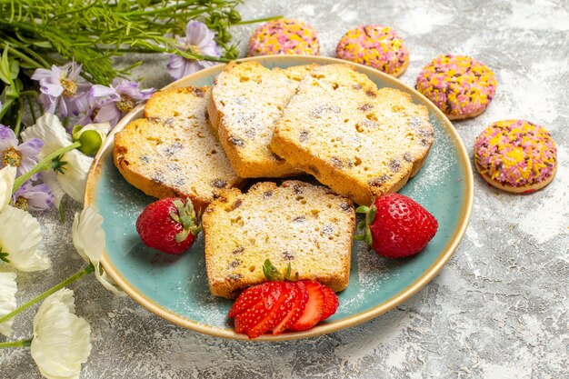 Vista frontal deliciosas rebanadas de pastel con fresas y galletas en pastel de superficie ligera pastel dulce