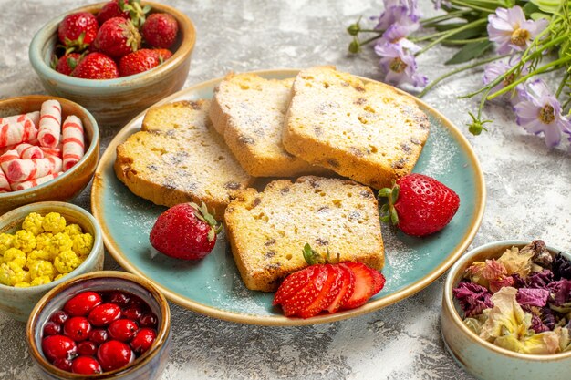 Vista frontal deliciosas rebanadas de pastel con fresas en superficie ligera pastel de pastel dulce de frutas