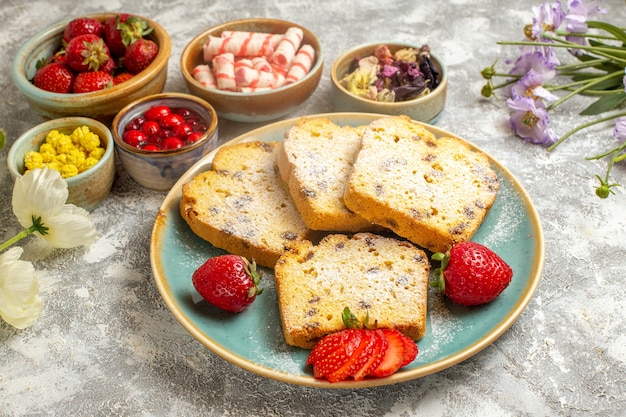 Vista frontal deliciosas rebanadas de pastel con fresas en superficie ligera pasteles dulces de frutas